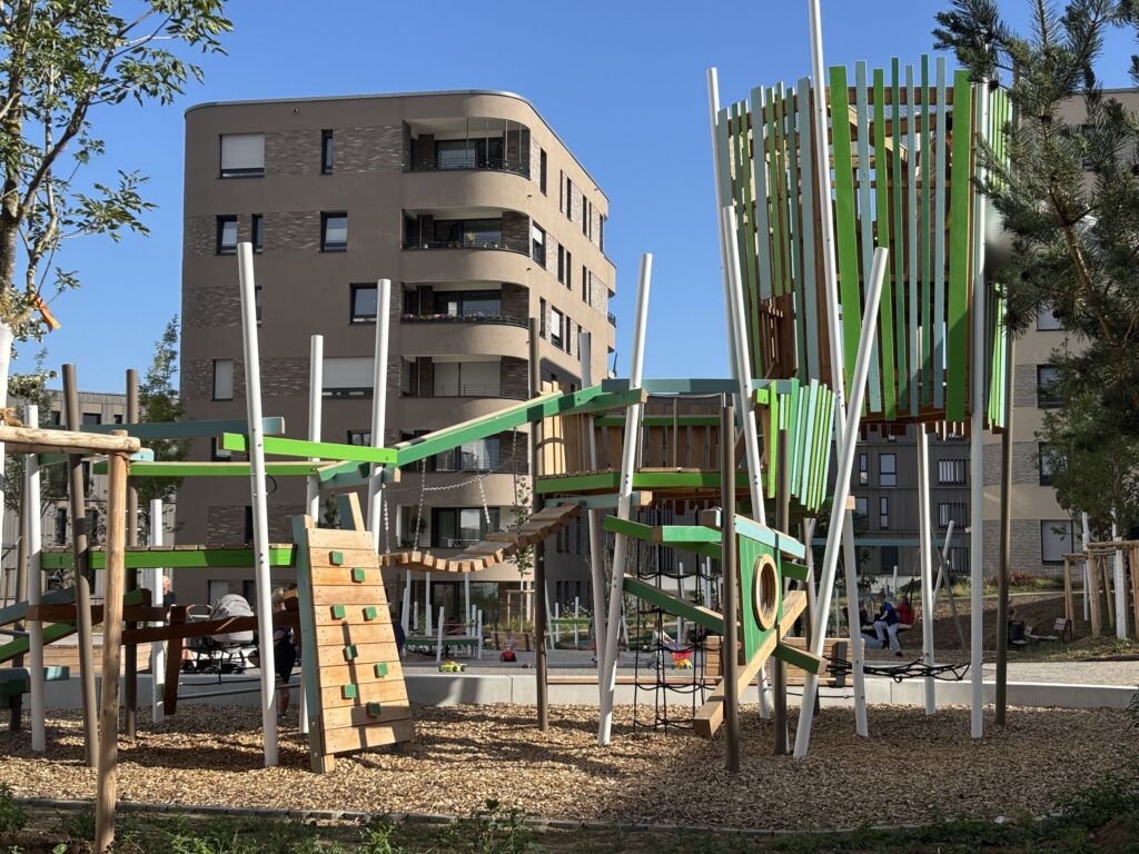 Moderner, farbenfroher Spielplatz mit hölzernem Klettergerüst im Innenhof des neugebauten Wohnquartiers Hochgelegen
